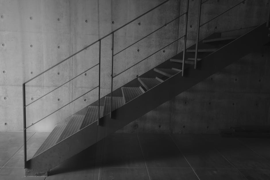 콘크리트 벽을 배경으로 한 산업용 금속 계단의 흑백 사진.