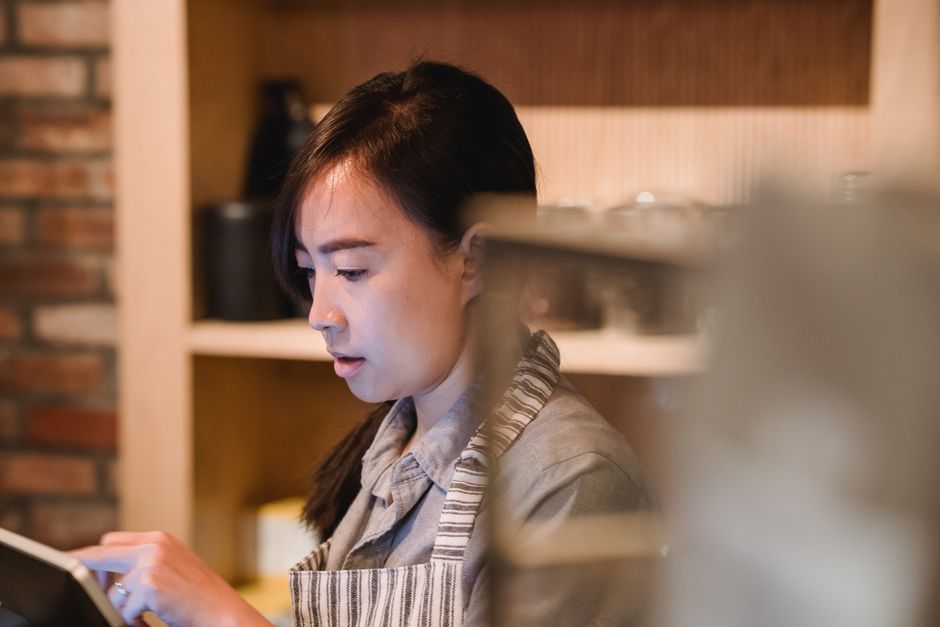 따뜻한 카페 분위기 속에서 사장님이 직접 스마트폰으로 글을 작성하는 모습